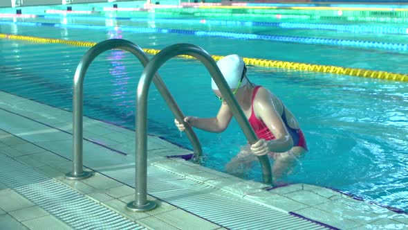 Side View Young Woman Swimmer Comes Out of Indoor Swimming Pool with Blue Water, Slow Motion, alt