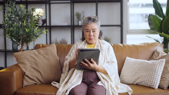 Asian mature woman using tablet in livingroom at home.