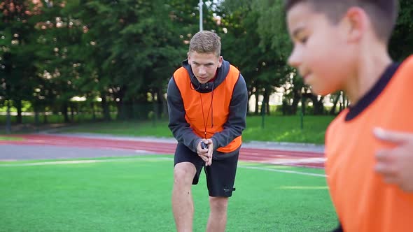 Football Trainer Controling the Time While His Skillful Pupils do Speed Exercises on Outdoors alt