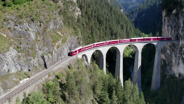 Aerial View of a Moving Red Train Along the Landwasser Viaduct in Swiss Alps alt