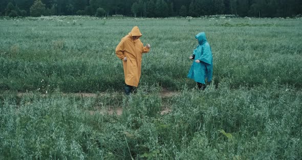 Man in a Yellow Raincoat and a Woman in a Blue Raincoat Dance a Twist in a Field