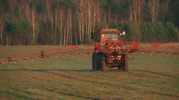 Tractor with a Sprayer Applies Fertilizer to Young Wheat Crops alt