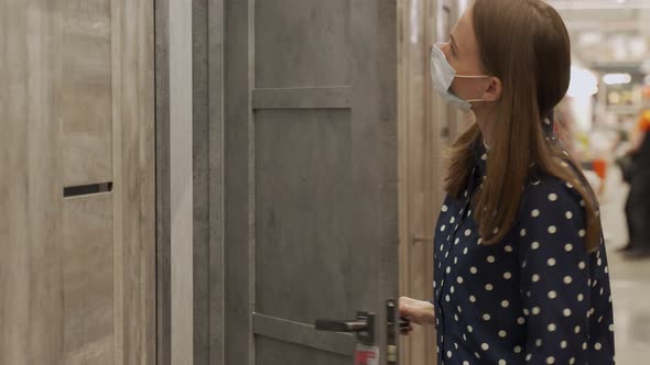 Woman Wearing a Protective Mask in a Store Buys a Wooden Door for a New House alt