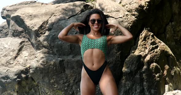 Beautiful fit playful black woman in bikini on volcanic beach.