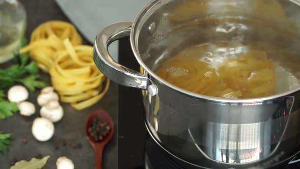 Hands Put Fettuccine Pasta in Pan of Boiling Water and Stir with Spoon