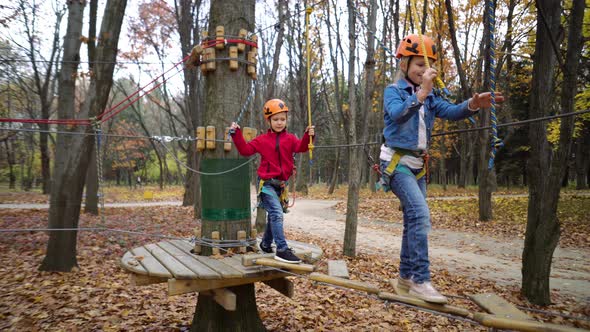 Rope Park. Two little girls in orange helmets in adventure park in safety equipment in autumn day.