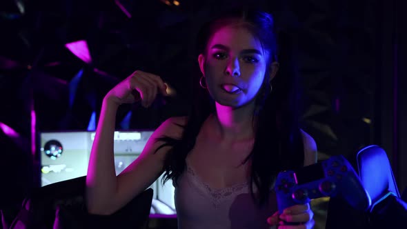 Young Woman Holding a Joystick in Neon Gaming Club and Blows a Bubble Gum - Laughing alt