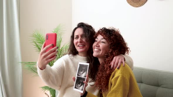 LGBT lesbian couple holding ultrasound photo scan on video call of growing baby in pregnancy time alt