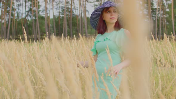 Young Woman in Dress and Hat Standing in Wheat Field alt