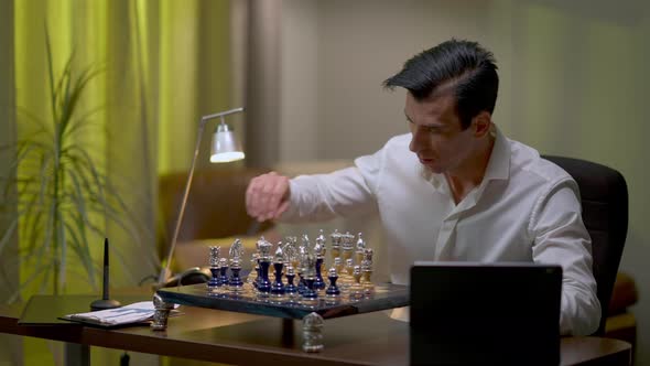 Thoughtful Young Middle Eastern Man Playing Chess at Home Checking Online Video alt