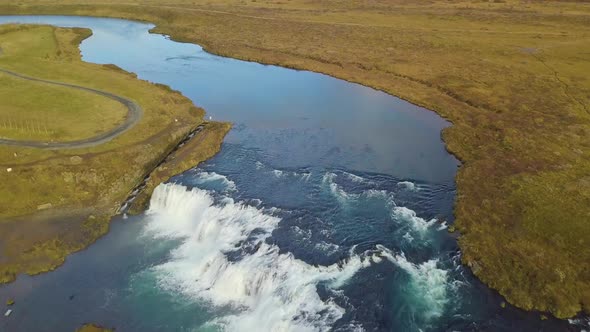 Drone view tilting up from Faxi Waterfall to reveal the Icelandic landscape alt