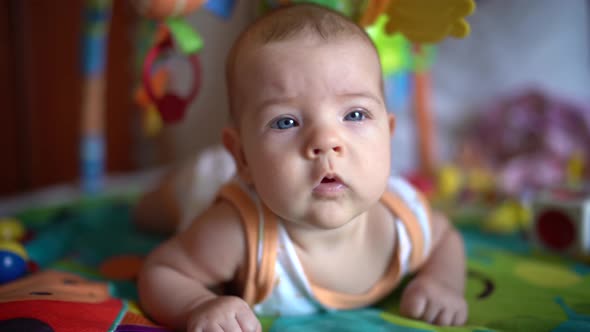Newborn Lies with Its Tummy on the Play Mat and Looks Around alt