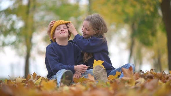 Cute Little Children in a Beautiful Autumn Park Play Sitting on Yellow Fallen Leaves.