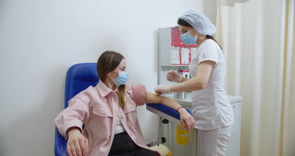 Medical Nurse in Safety Gloves and Protective Mask is Making a Vaccine Injection to a Female Patient