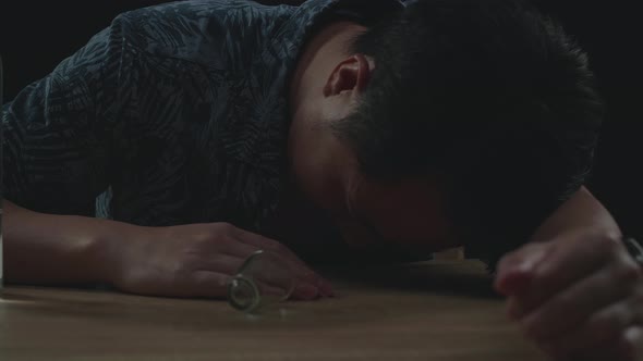 Drunk Asian Man Pouring Vodka In A Shot Glass Before Drinking And Sleeping In Black Background alt