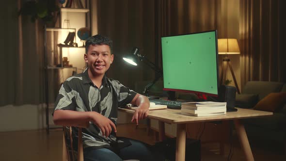 Asian Boy Learning Online With Mock Up Computer Green Screen From Home, He Turns And Warmly Smiles alt