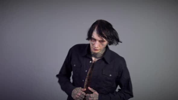 Confident Man with Naked Tattooed Torso in Black Shirt Sitting Down on Chair Looking at Camera alt