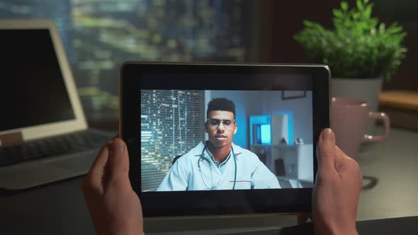 Tablet Screen with Handsome Multiracial Doctor Speaking with Patient Online