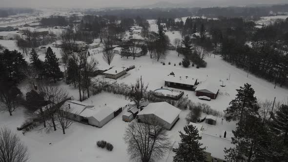 Aerial view over snow covered residential neighborhood with lots of pine trees. Gray cloudy sky.