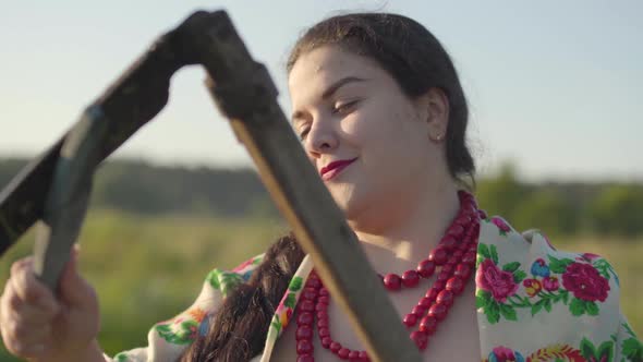 Overweight Woman Sharpening Scythe Preparing To Start Mow on the Green Summer Field alt