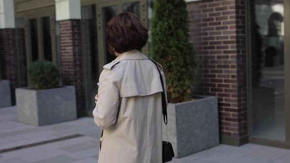 Cute Woman Chatting in Smartphone in Trench Coat, Back View 