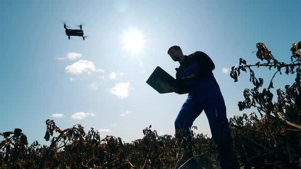 Male Agronomist Is Operating a Drone From the Laptop alt