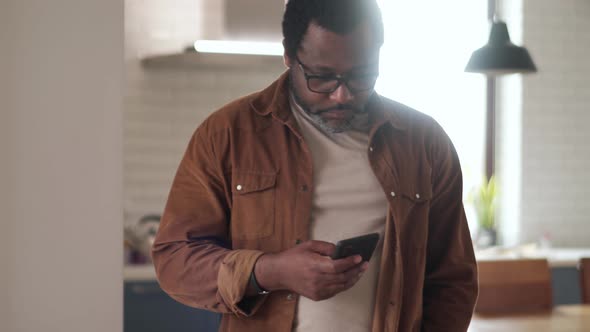 Pensive African man typing by phone alt
