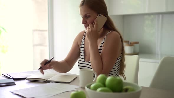 Woman Talking on Phone and Working at Table in Home Kitchen Indoors Spbd alt