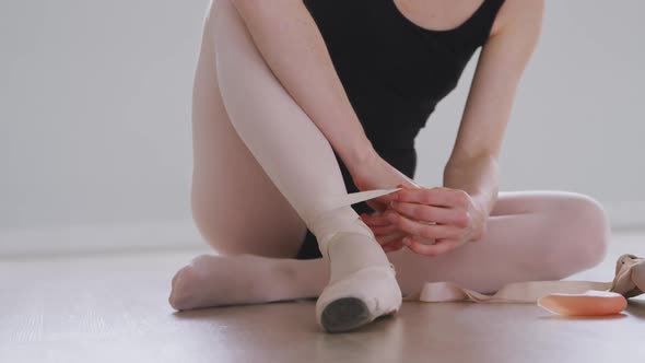Caucasian female ballet dancer sitting on the floor in the studio and tying her ballet shoes alt