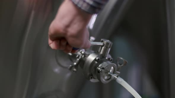 Close-up of a Male Brewer Opening a Tap for Dispensing Beer From a Beer Tank To a Keg alt