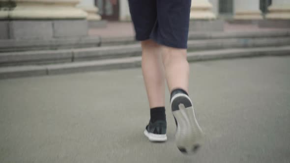 Camera Follows Caucasian Boy Running To School in the Morning. Back View of Cheerful Little alt