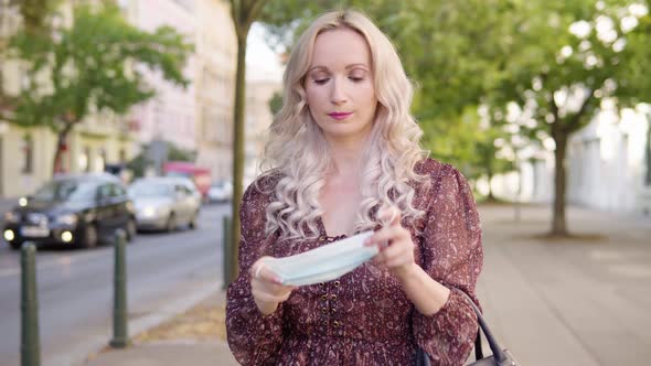 A Middleaged Caucasian Woman Takes Off a Face Mask and Smiles at the Camera in an Urban Area alt