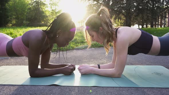 Fit female athletes doing plank exercise in park alt
