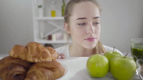 Portrait of Beautiful Slim Girl Choosing Between Green Apples and Crusty Croissants alt
