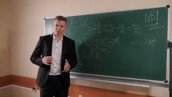 A Portrait of a Male Professor Standing Against a Blackboard with Chalk alt