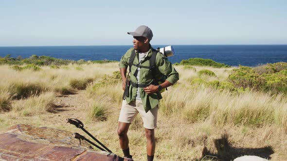 African american man hiking in countryside by the coast taking a rest alt