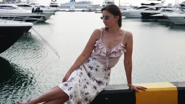 Girl in Sunglasses and a Dress Stands in the Seaport alt