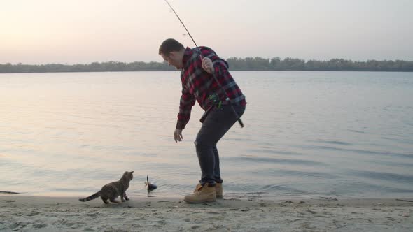 Male Angler Catching Fish Near Cat in Morning