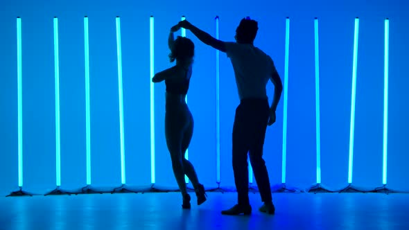 Dancers Practice a Series of Spins Against a Backdrop of Bright Blue Neon Lights in a Dark Studio alt