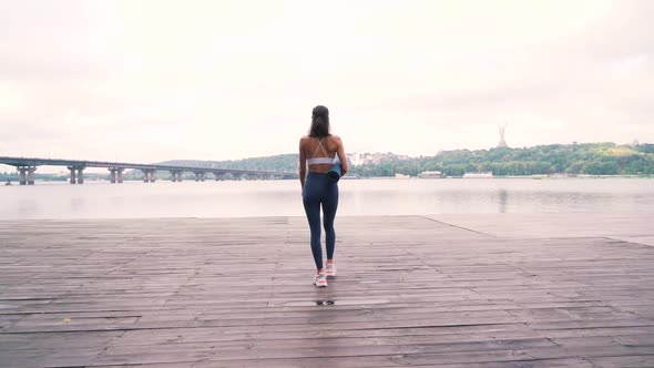 Girl with a Fitness Mat Walks Along the Pier