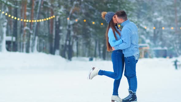 Cute Couple in Blue Sweaters Hugs and Kisses on Skating Rink
