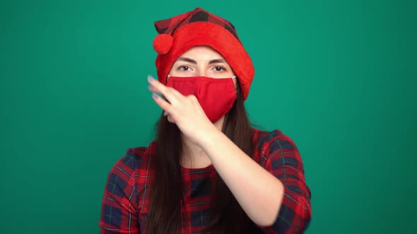 Portrait of Pretty Woman Wearing Christmas Red Hat and Medical Protective Face Mask Showing Zip alt