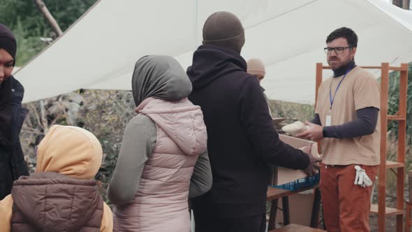 Refugees Accepting Food and Clothes from Social Workers alt