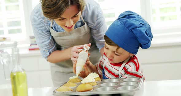 Mother helping boy to decorate cupcake with cream alt