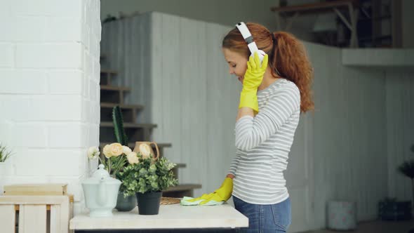 Happy Young Housewife in Rubber Gloves Is Listening To Music Through Headphones and Singing During alt
