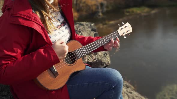 Caucasian Woman Sits on Rock and Plays the Ukulele