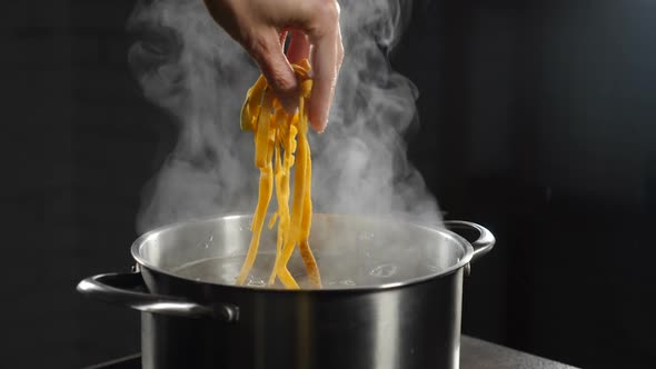 Female Chef Putting Raw Pasta Into Boiling Water, White Smoke in Slow Motion Rising Above Hot alt