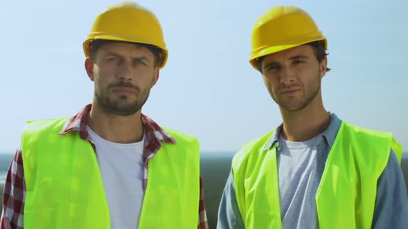 Professional Builders in Uniform and Safety Helmets Seriously Looking at Camera