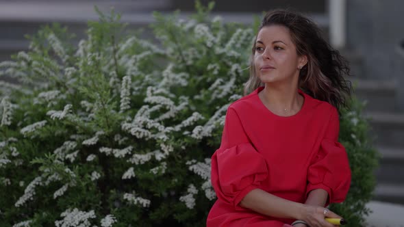 Middle Aged Woman is Smoking Outdoors in City Alone Sitting on Bench Exhaling Smoke From Ecigarette alt