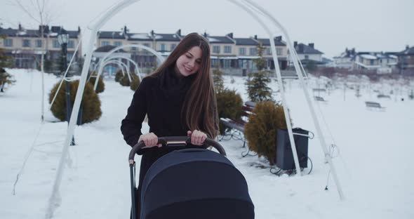 Mom Walks With The Baby In A Stroller On A Snowy Street